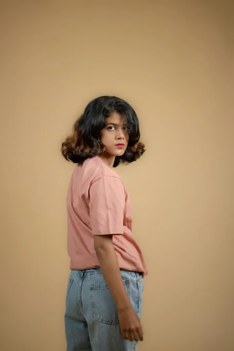 a young girl standing in front of a brown wall
