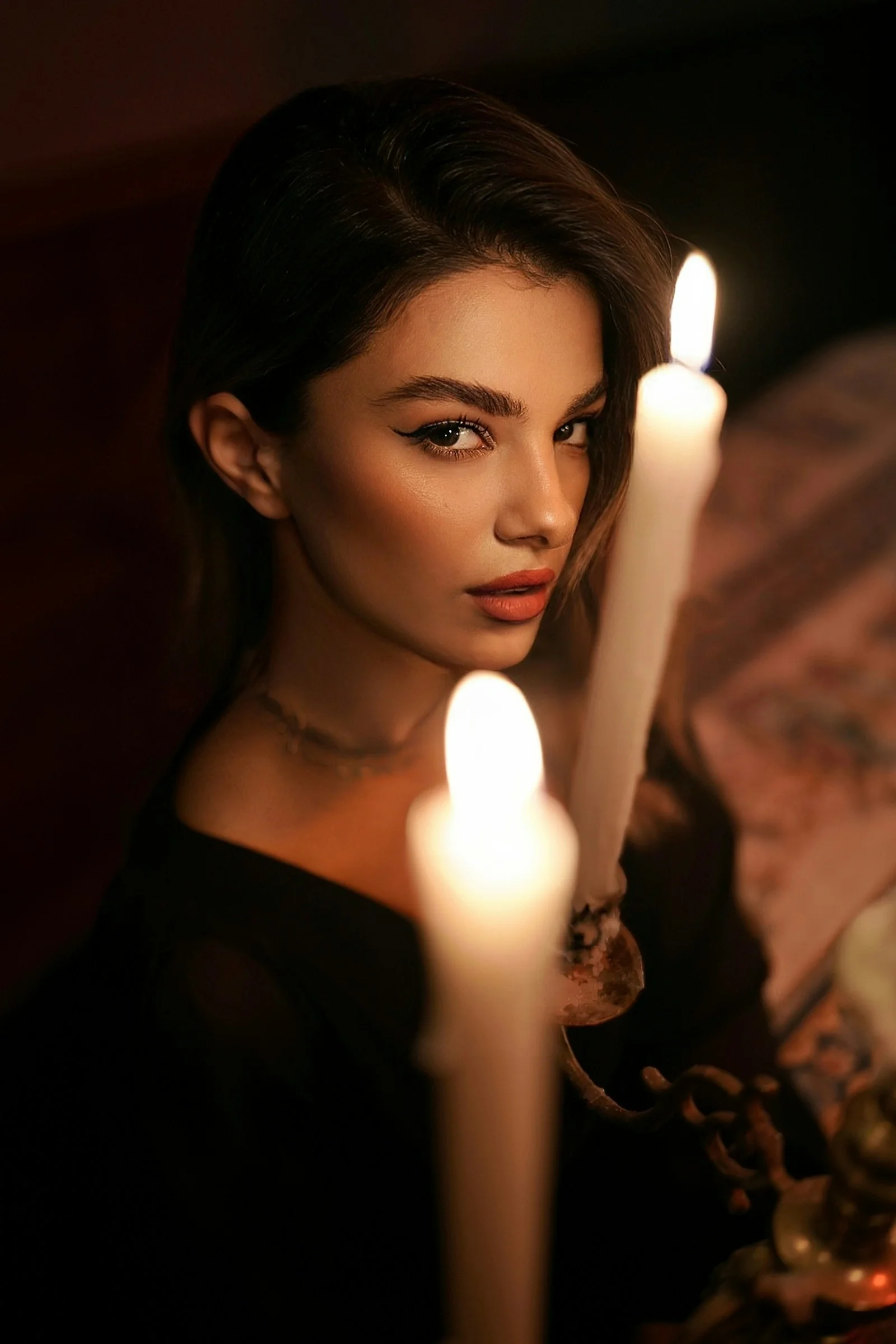 A woman in a black top looking past two lit candles in a dark room