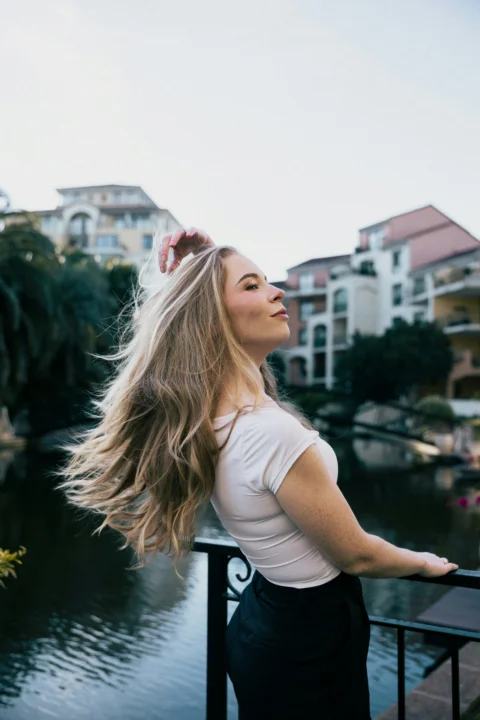 一位金色长发的女人靠在运河边的栏杆上向后甩动头发