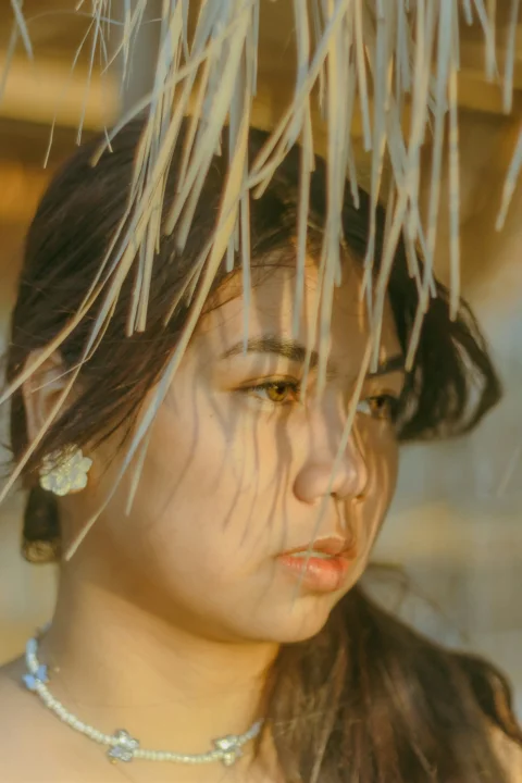 a woman wearing a necklace and earrings under a palm tree