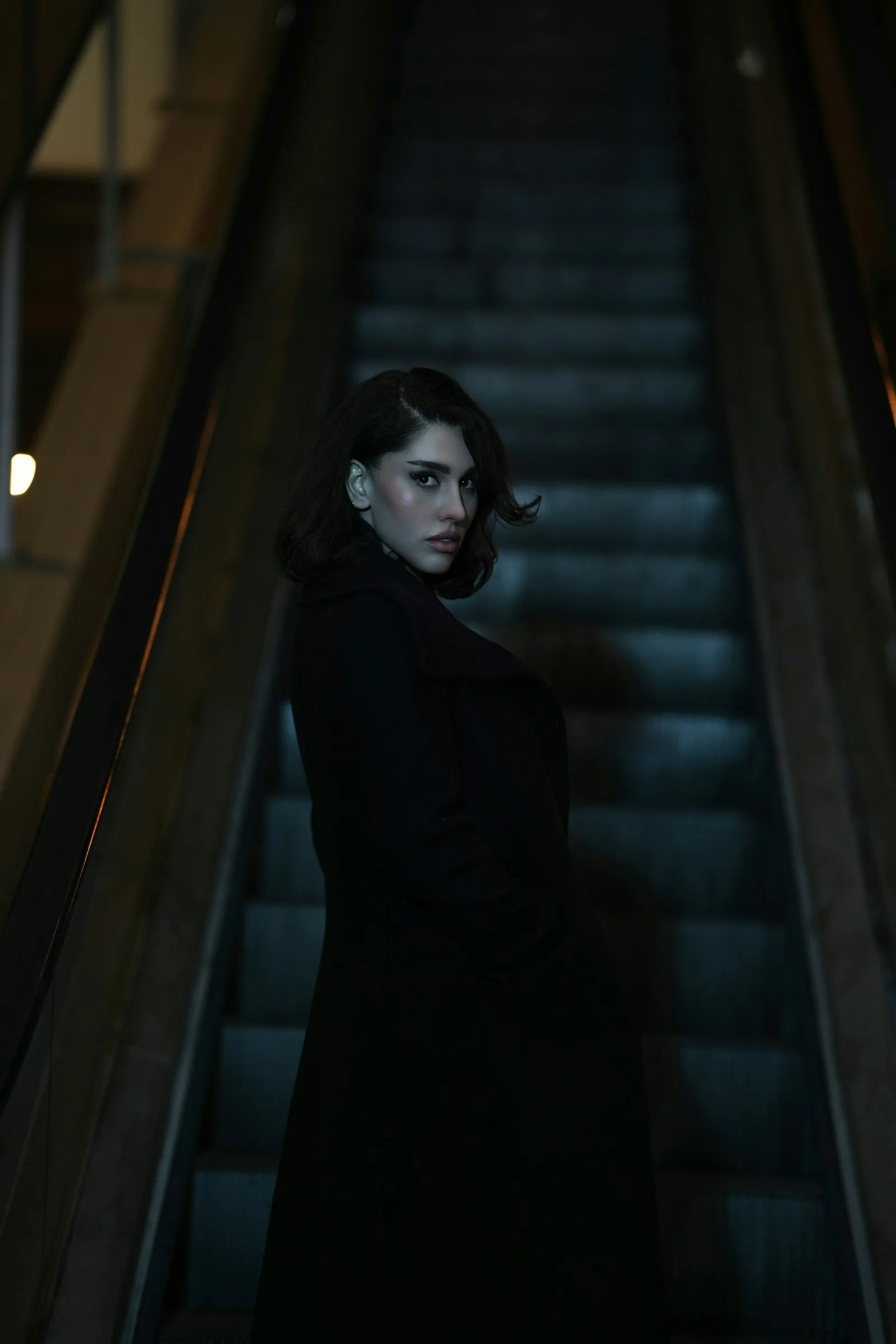 A woman stands on a dark escalator