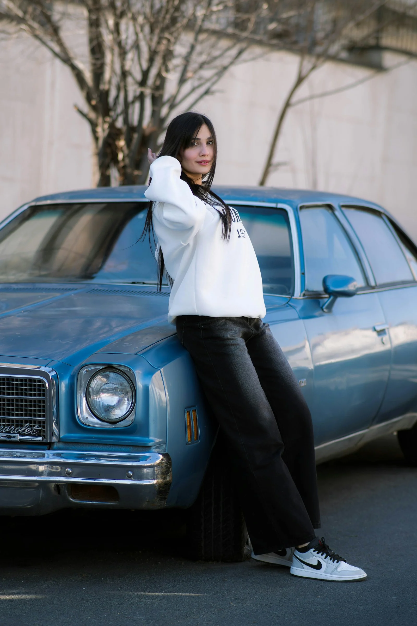 ヴィンテージの青い車にもたれる若い女性