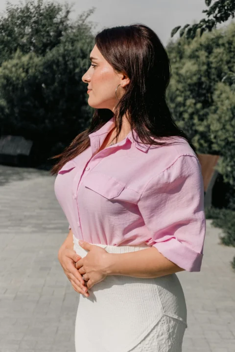 A woman in a pink button-down shirt and white skirt in a park