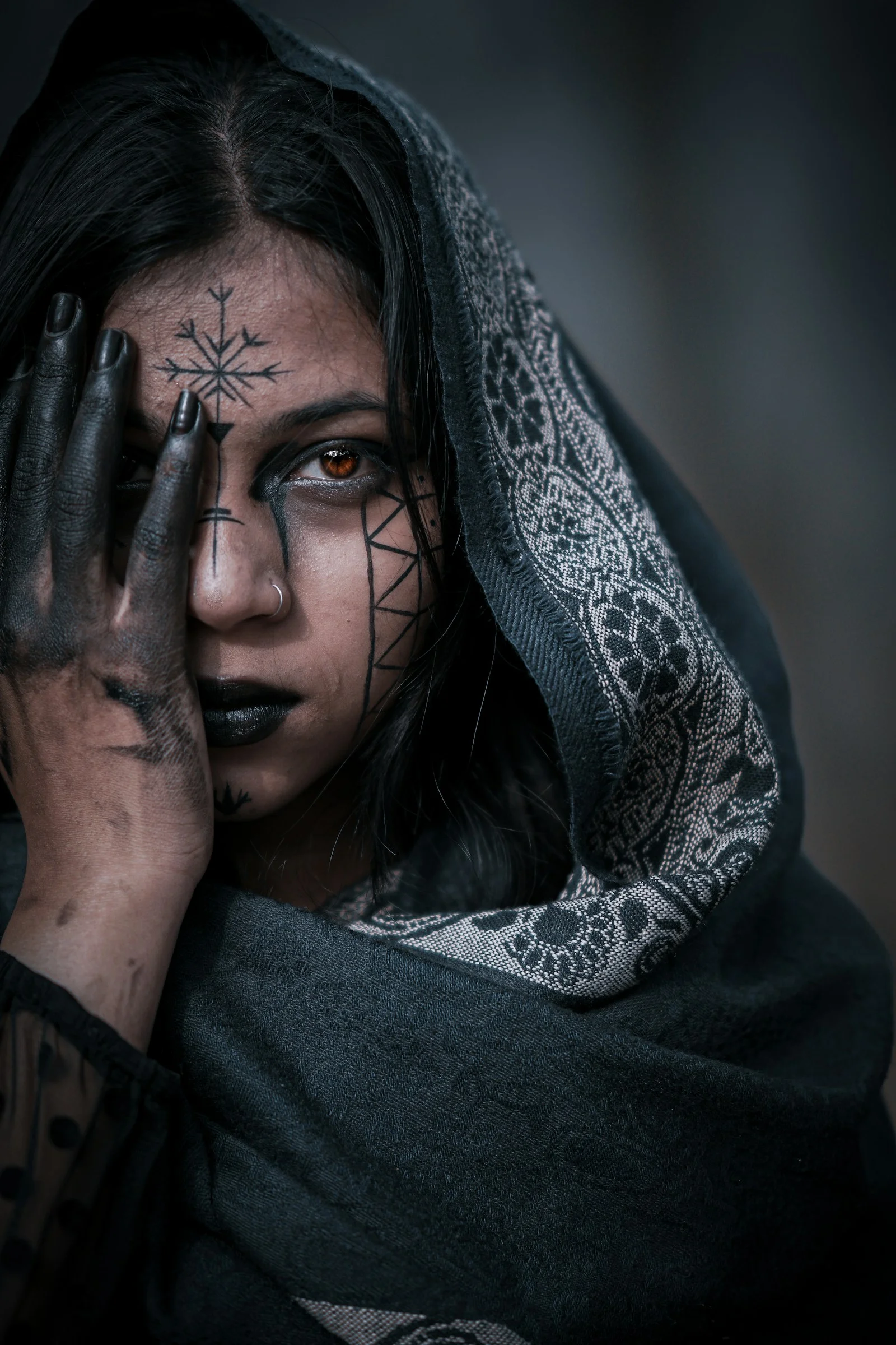 Woman with dark makeup and face paint covers eye