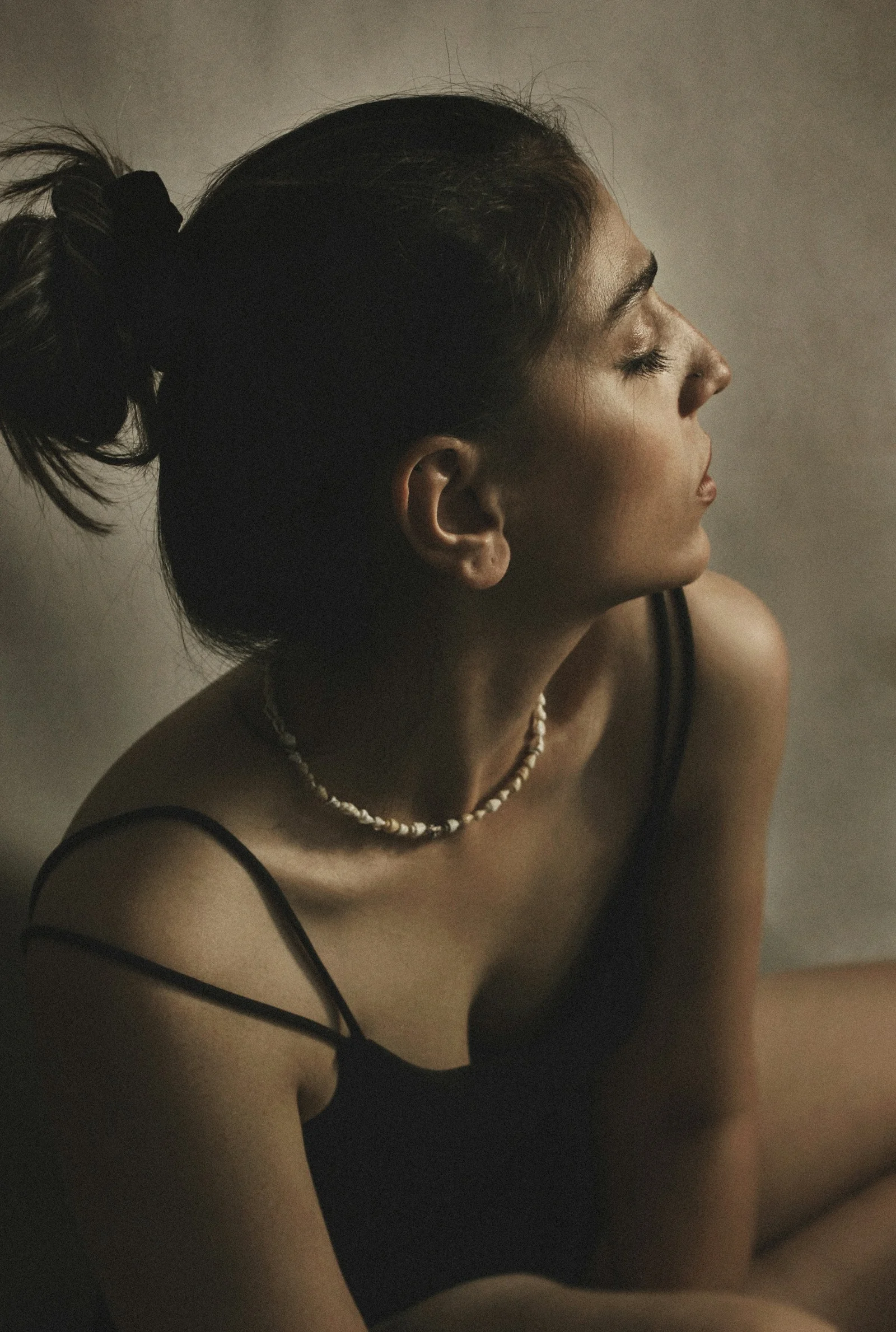 A woman with hair in a bun wearing a shell necklace