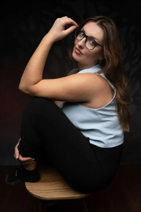 A young woman with glasses sitting on a wooden stool