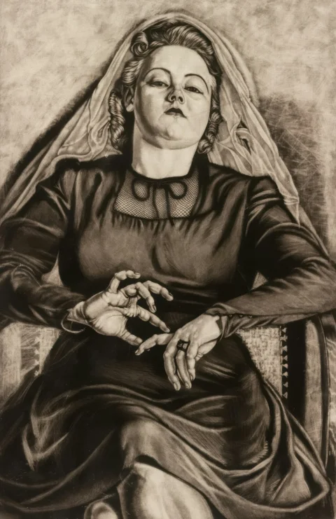 Woman in dark dress with veil sits with hands clasped