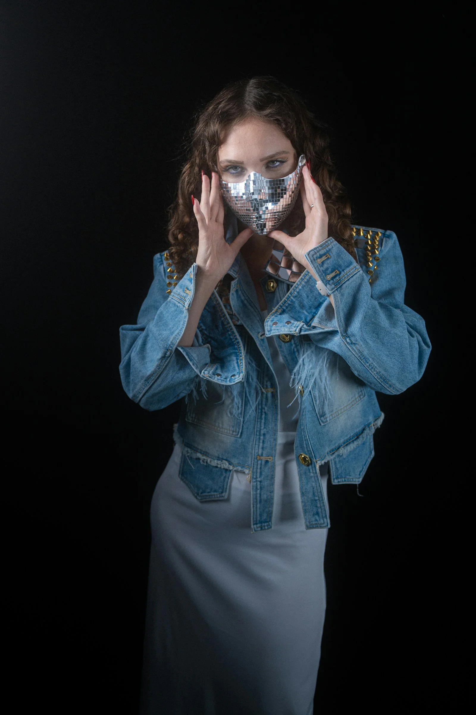 A woman wearing a reflective disco ball mask and a studded denim jacket