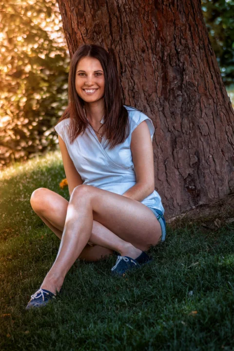 a woman sitting in the grass next to a tree