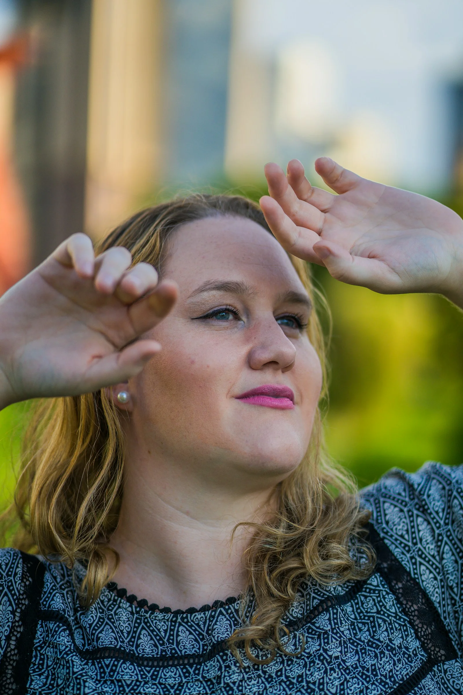 A woman with blonde hair shielding her eyes from the sun outdoors