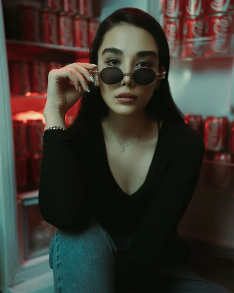 a woman wearing sunglasses sitting in front of a refrigerator