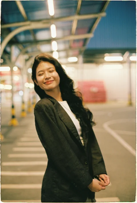 Young woman in blazer smiles outdoors at night