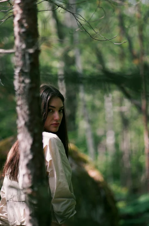 a woman standing in the woods with her back to the camera