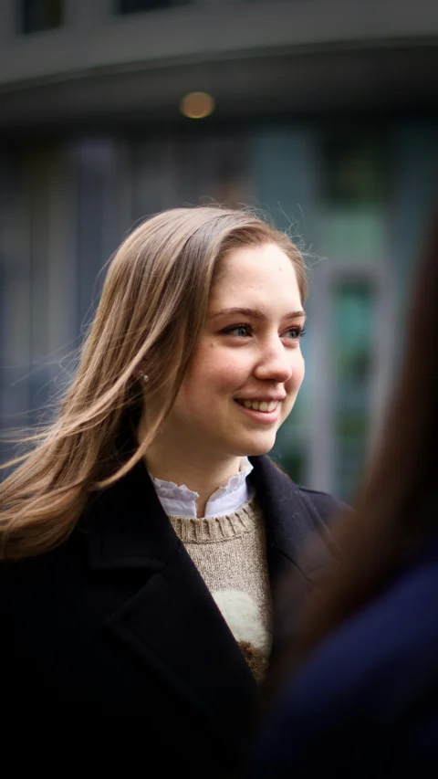 A young woman smiles outdoors, looking happily