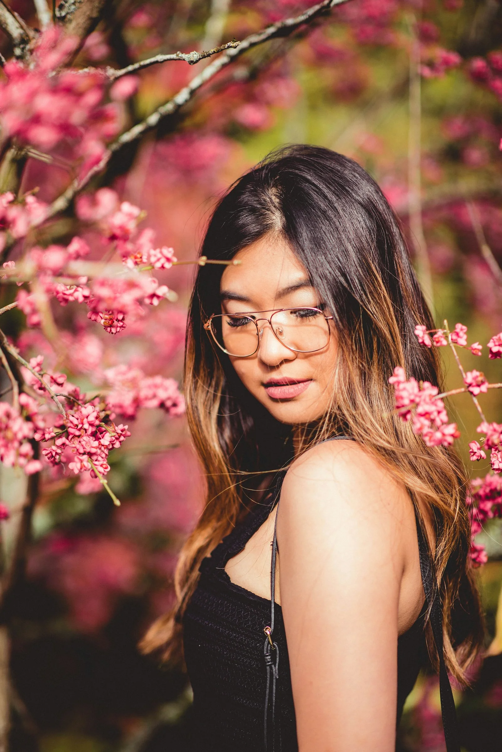 a woman wearing glasses standing in front of a tree with pink flowers