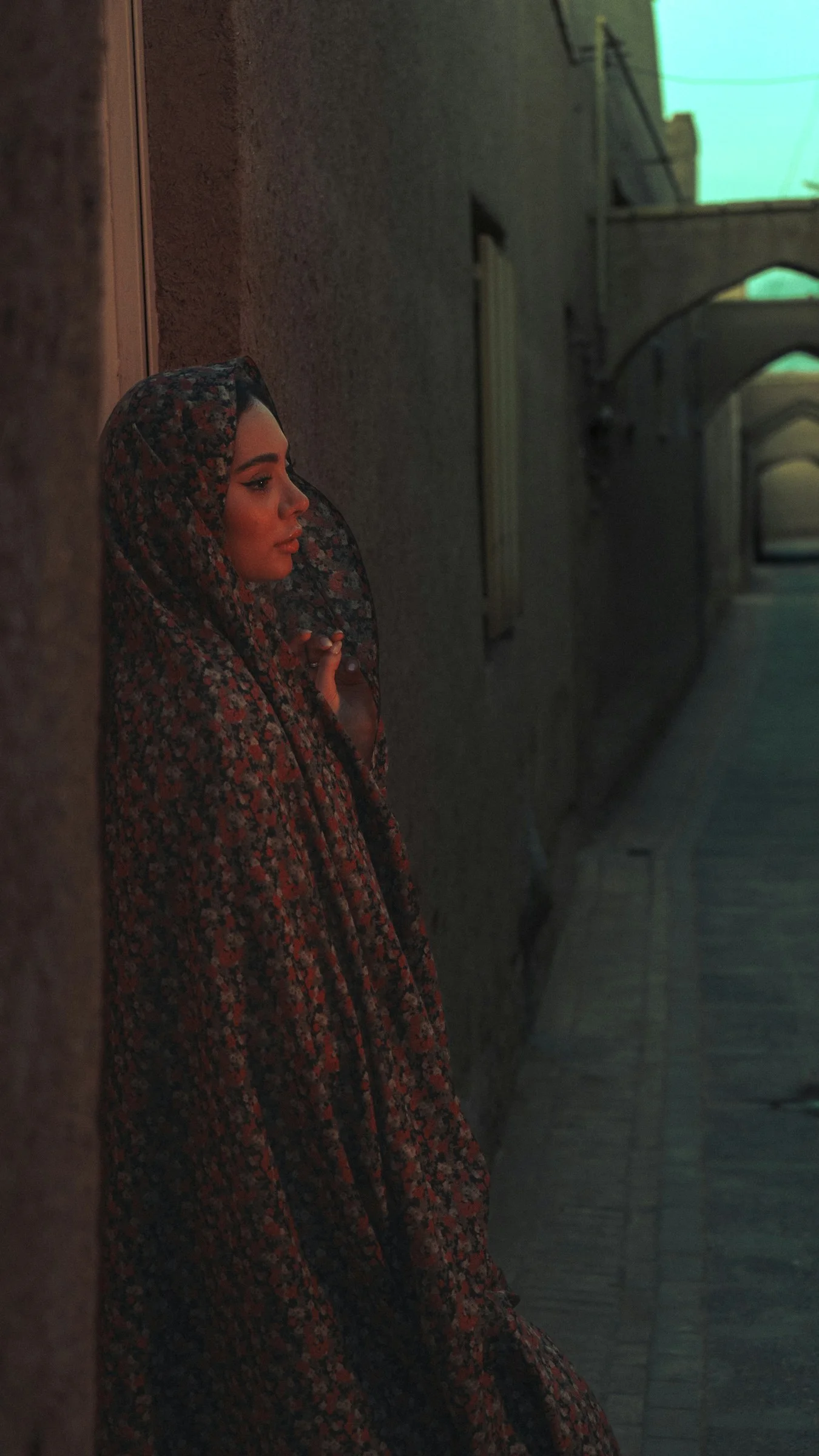 A woman in a hijab stands in a dim alley