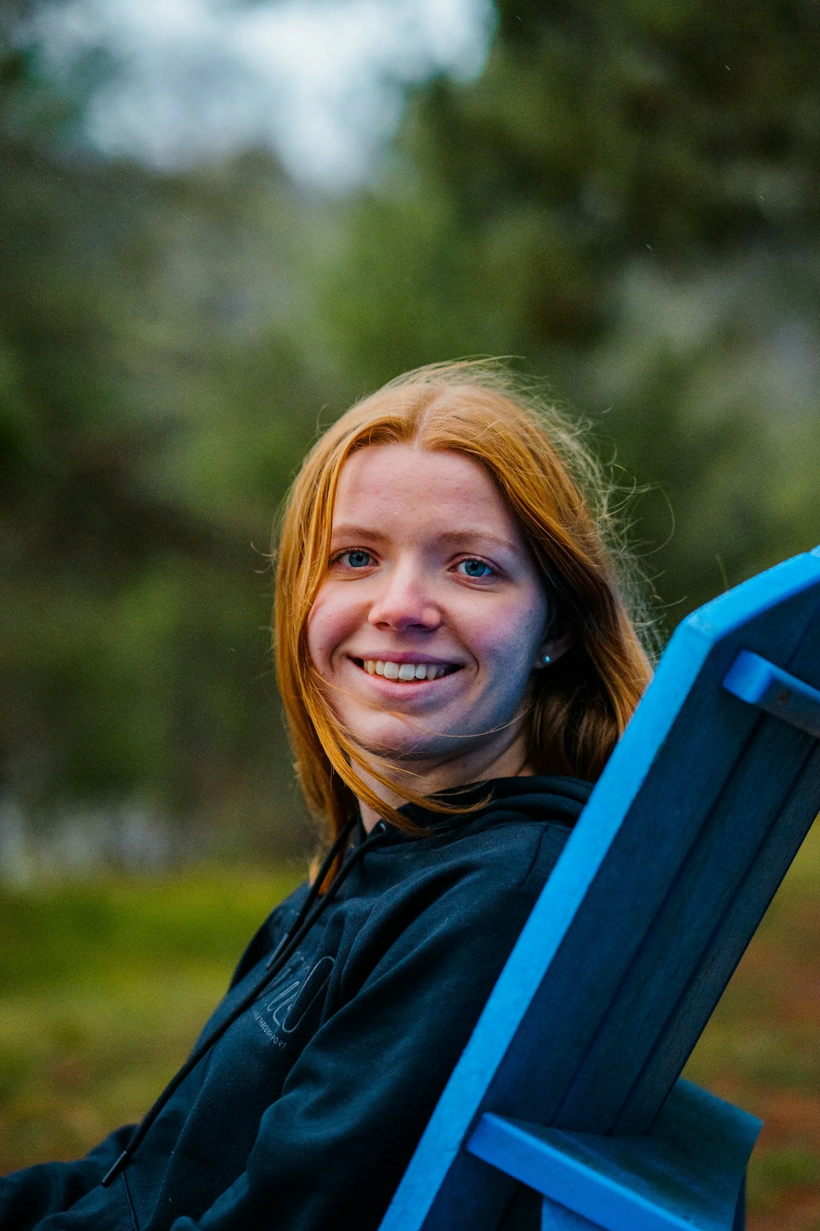 A woman with long red hair in a black hoodie sitting in a blue chair