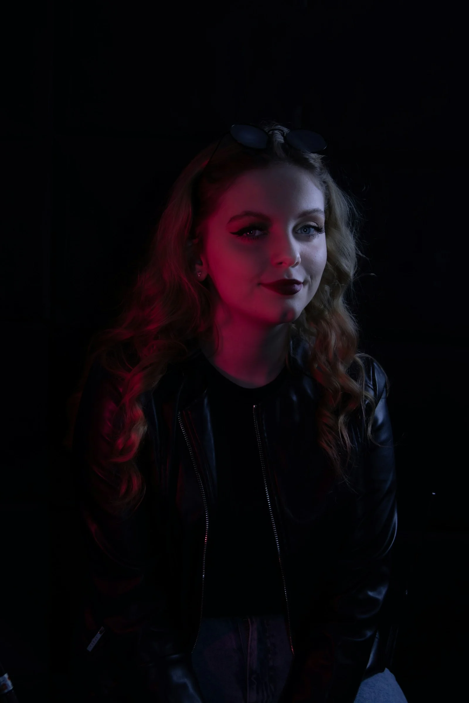 a woman in a black leather jacket sitting in a dark room