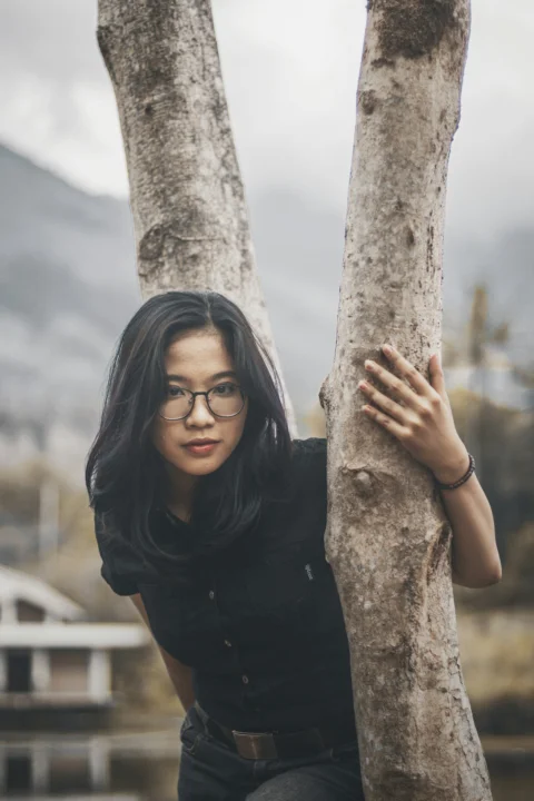 戴眼镜的女人倚靠在树上