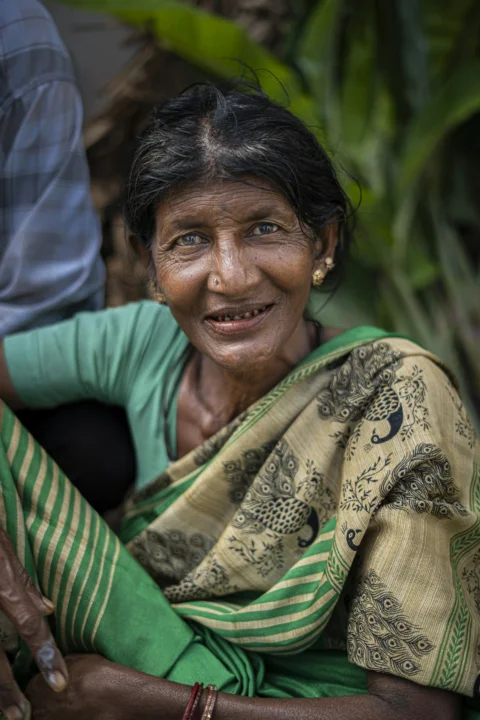 An elderly woman with a nose ring wearing a green and patterned sari