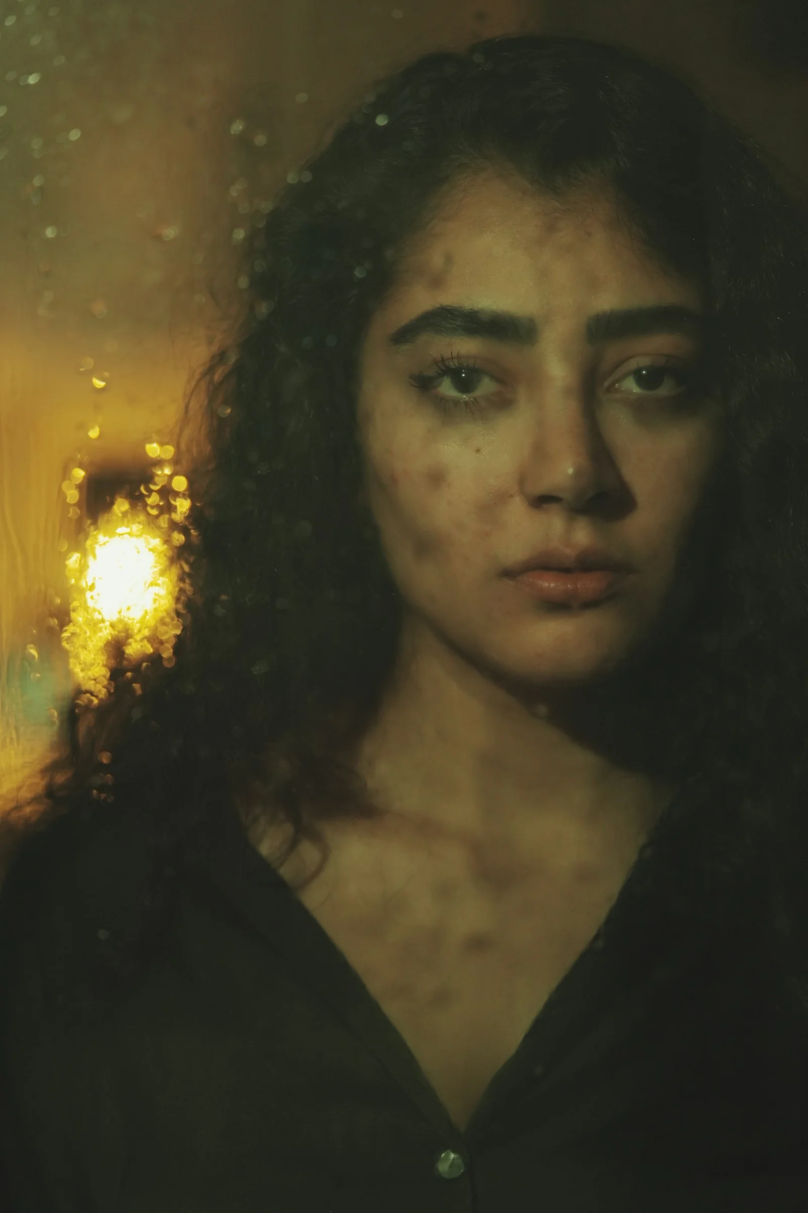 Woman looking through a rain-streaked window at night