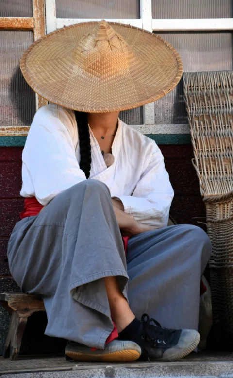 Person in conical hat sitting outdoors near woven baskets
