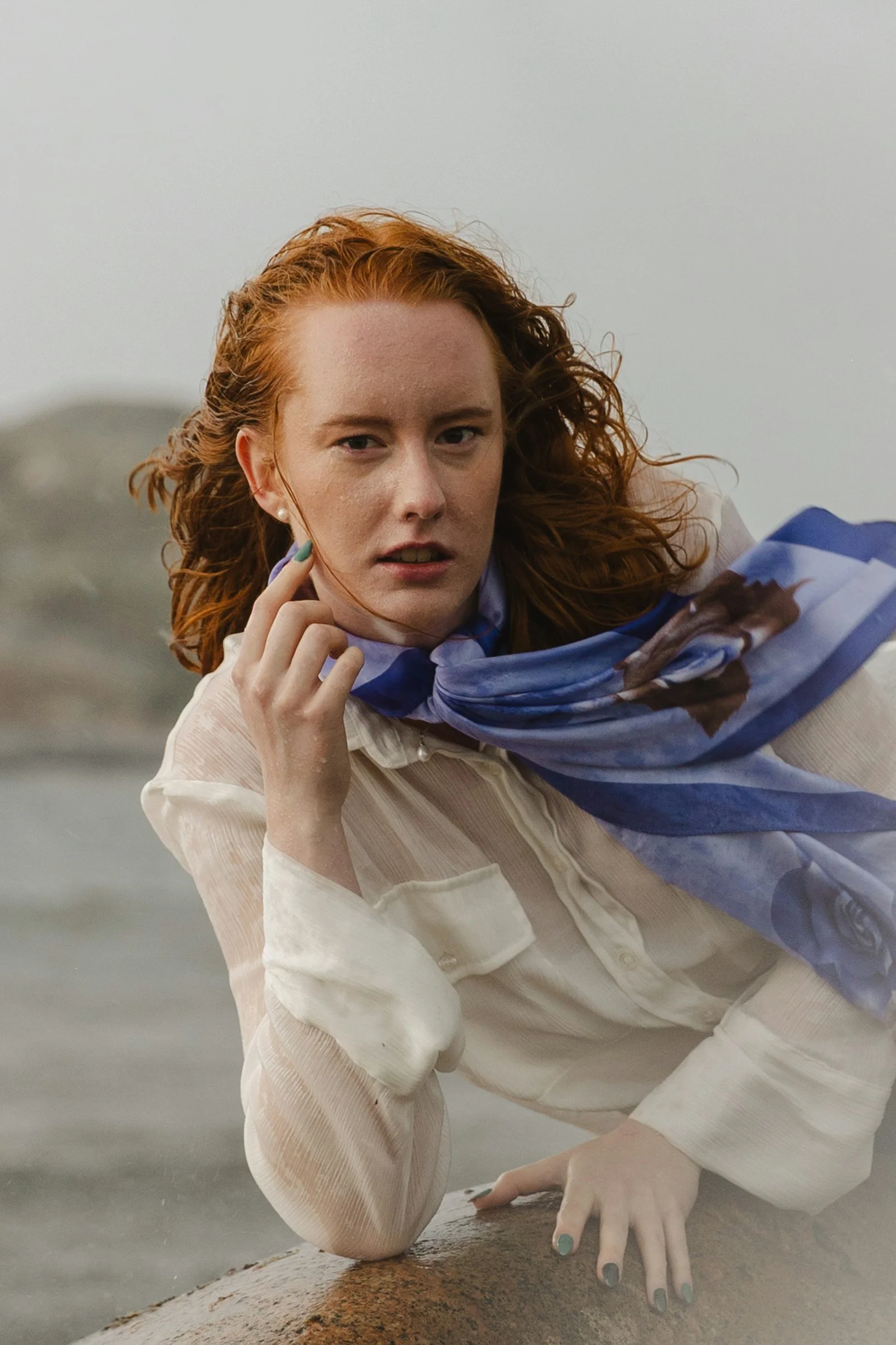 A woman with red hair wearing a white shirt and blue scarf outdoors
