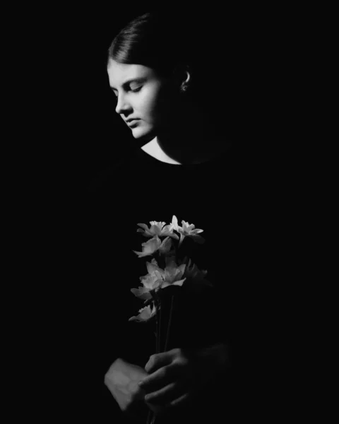 Young woman holding flowers in dramatic lighting