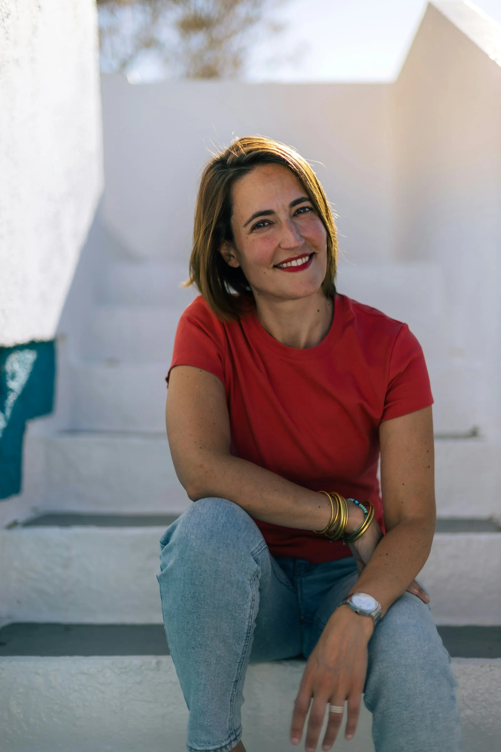 A woman in a red t-shirt and jeans sitting on white stairs