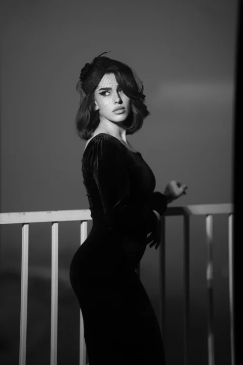 A woman in a black dress poses by a railing