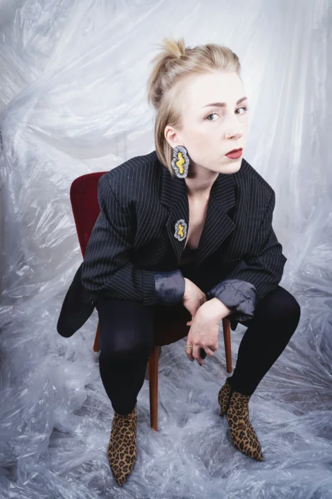 Woman in blazer and leopard print shoes sits on chair