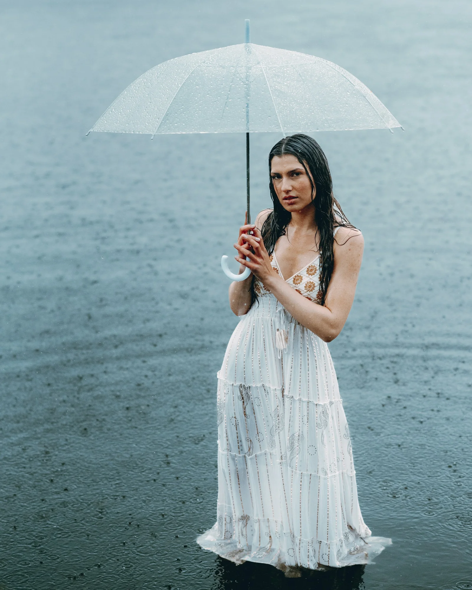 Woman stands in rain under umbrella