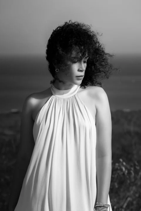 A woman with curly hair in a white halter dress outdoors in black and white