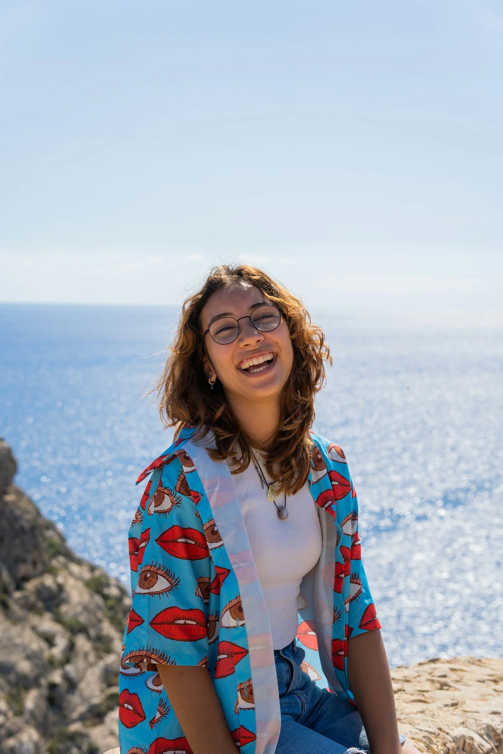 a woman sitting on top of a rock near the ocean