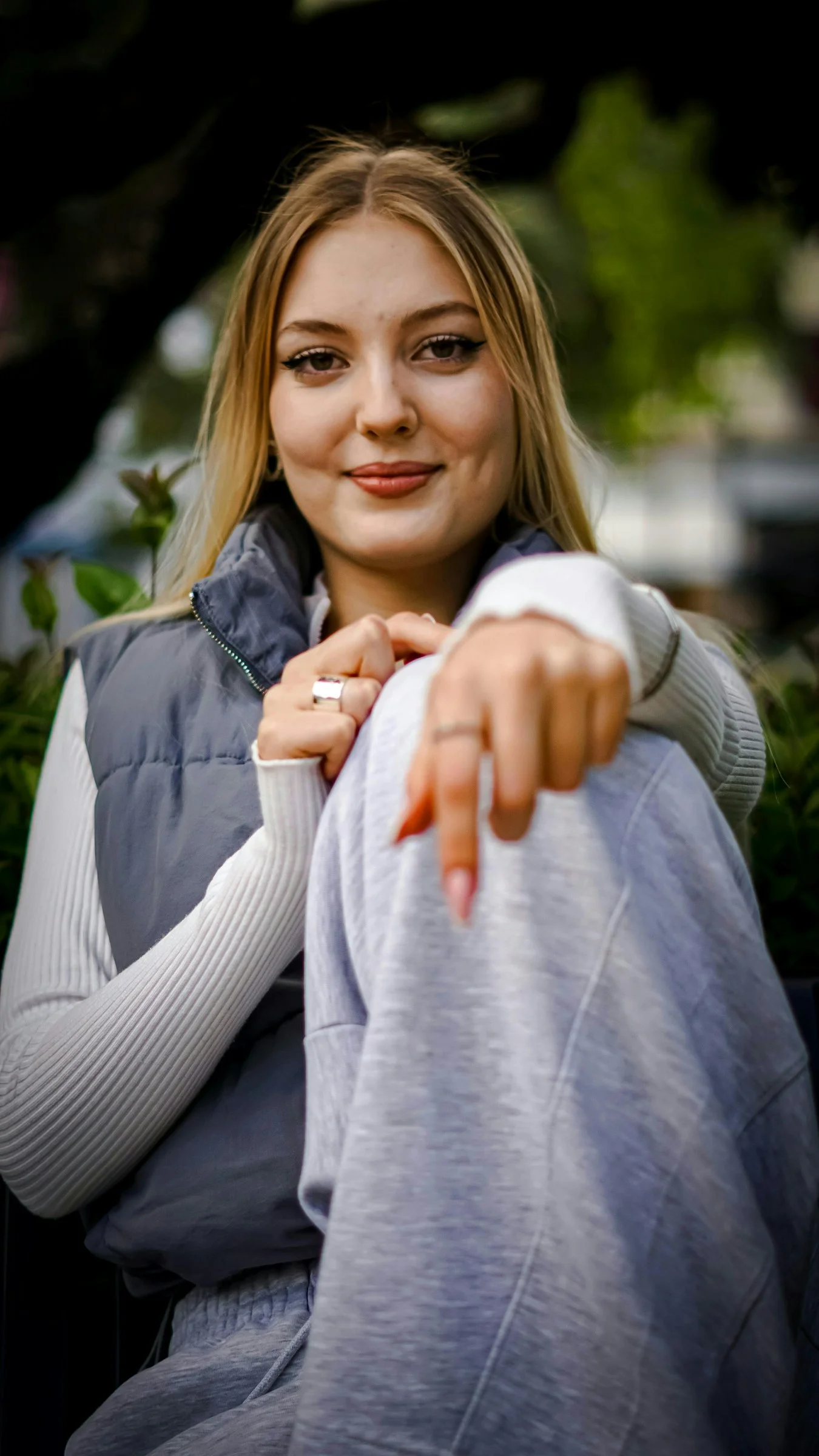 A smiling young woman is gesturing towards the camera