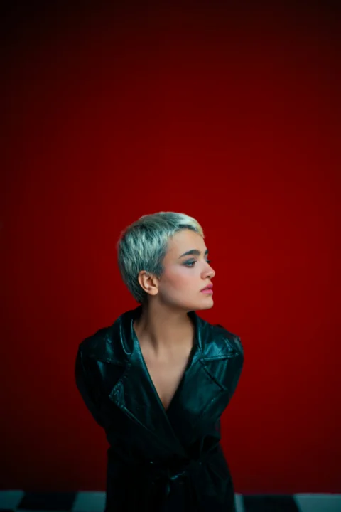 A woman in a black leather jacket standing in front of a red wall