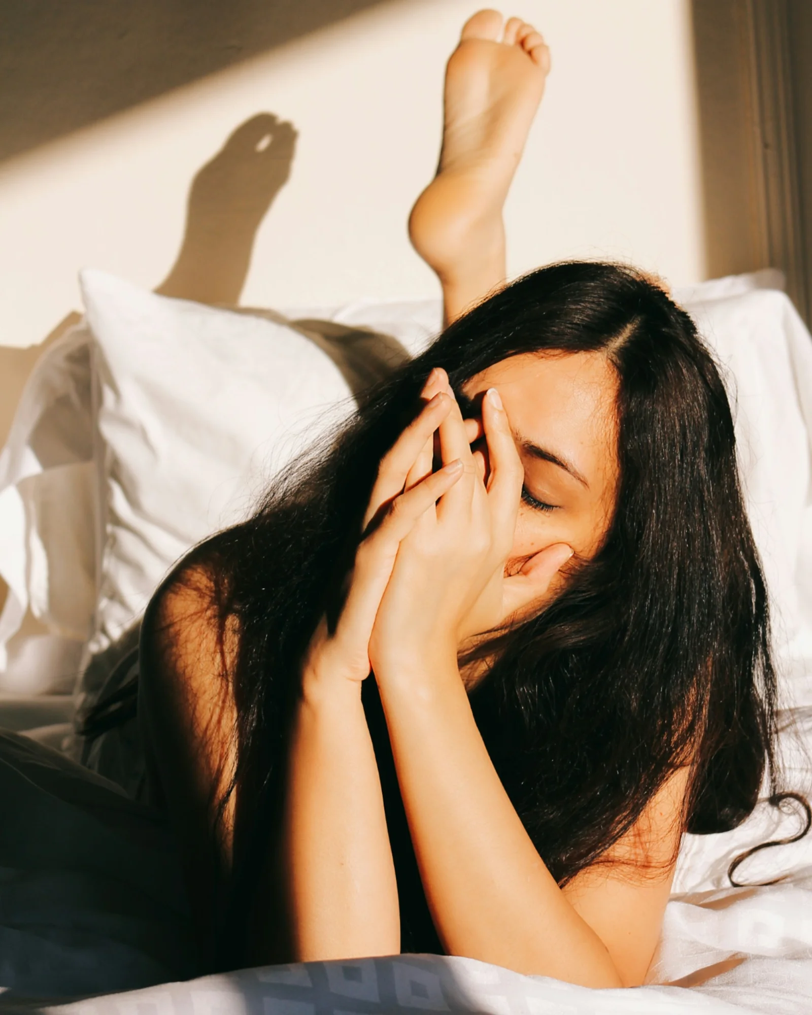 ベッドに横たわり顔に手を当てている女性