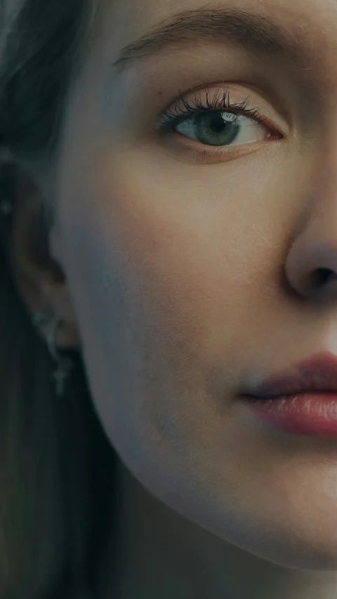 A close-up of a woman with green eyes and a silver cross earring