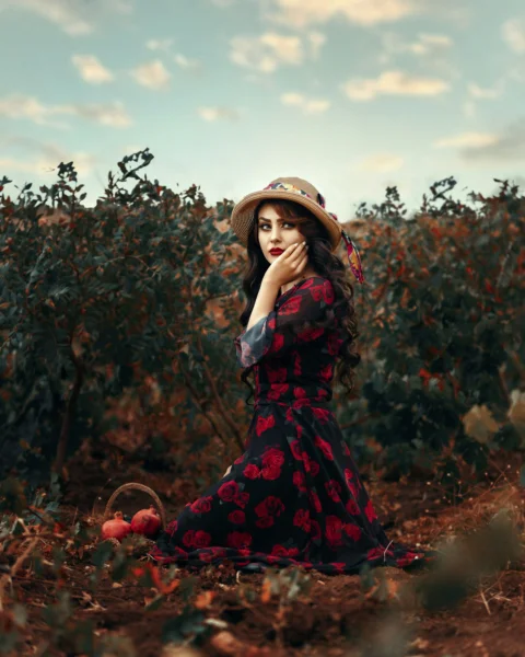 a woman in a red dress and hat sitting in a field