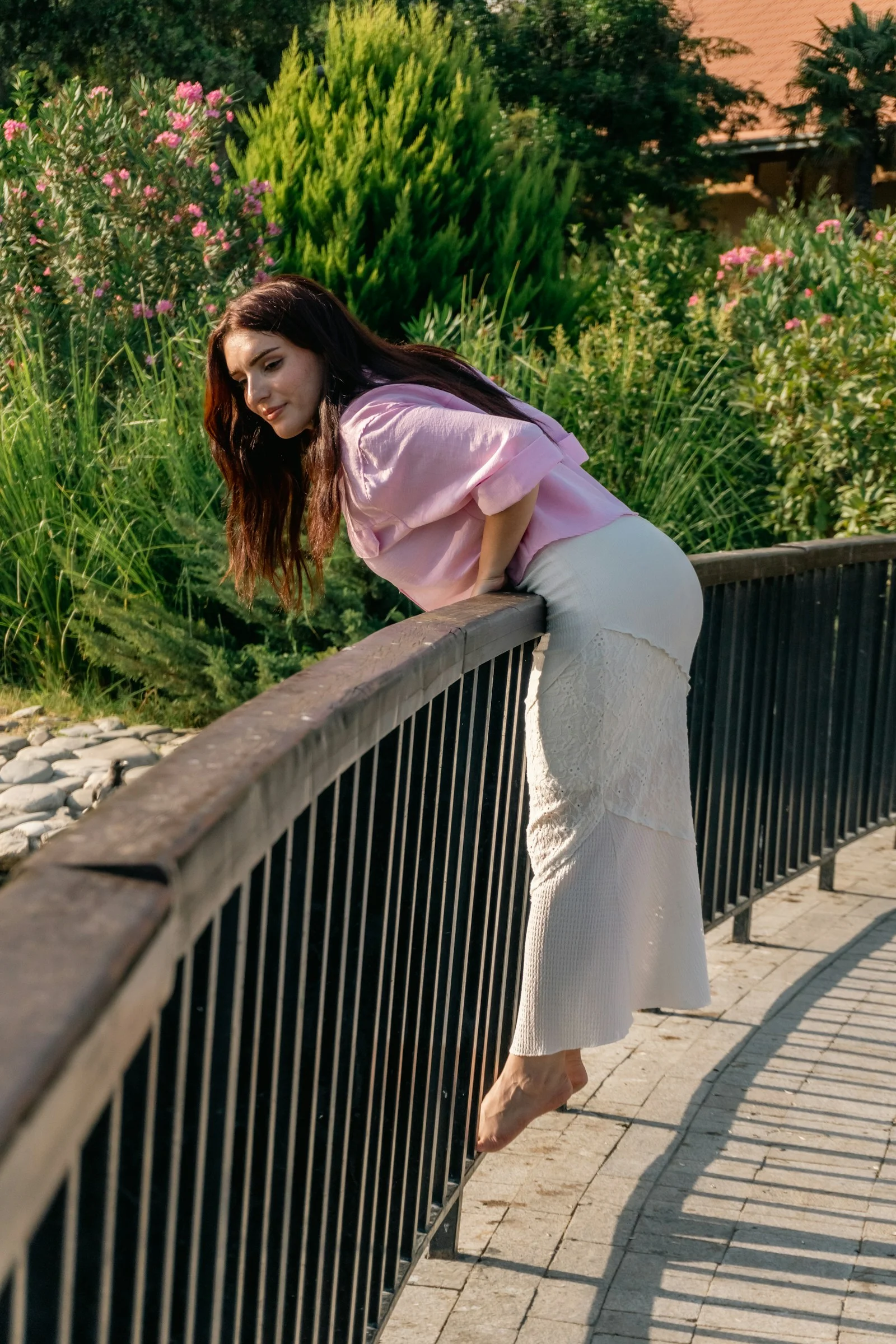 A woman in a pink shirt and white skirt leaning over a metal railing