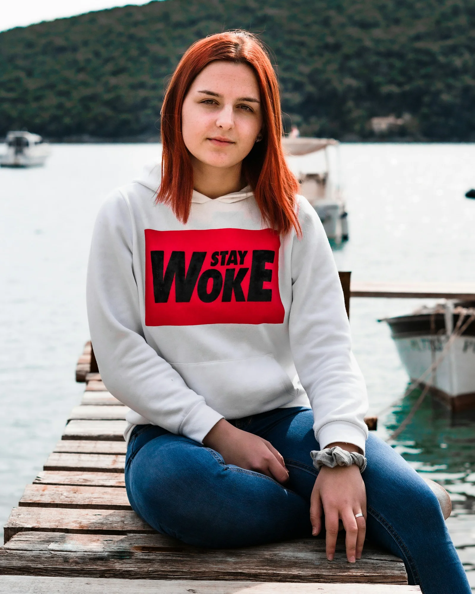 woman in white and red long sleeve shirt and blue denim jeans sitting on brown wooden