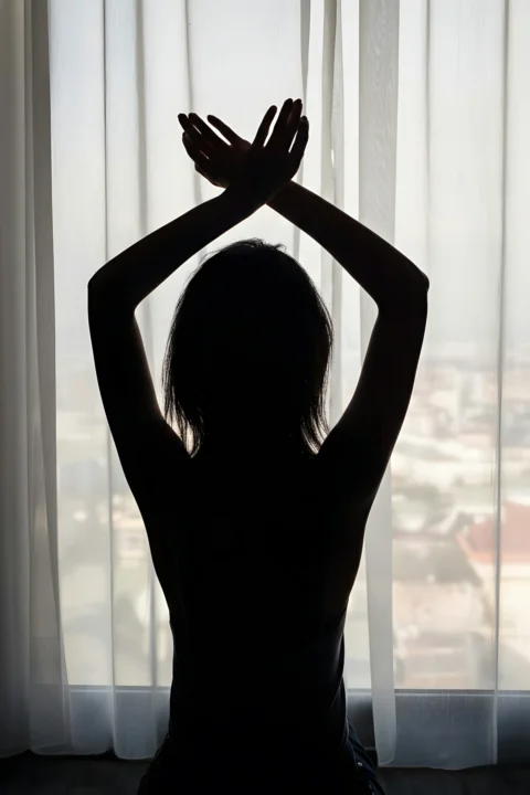 Silhouette of a woman with arms crossed overhead