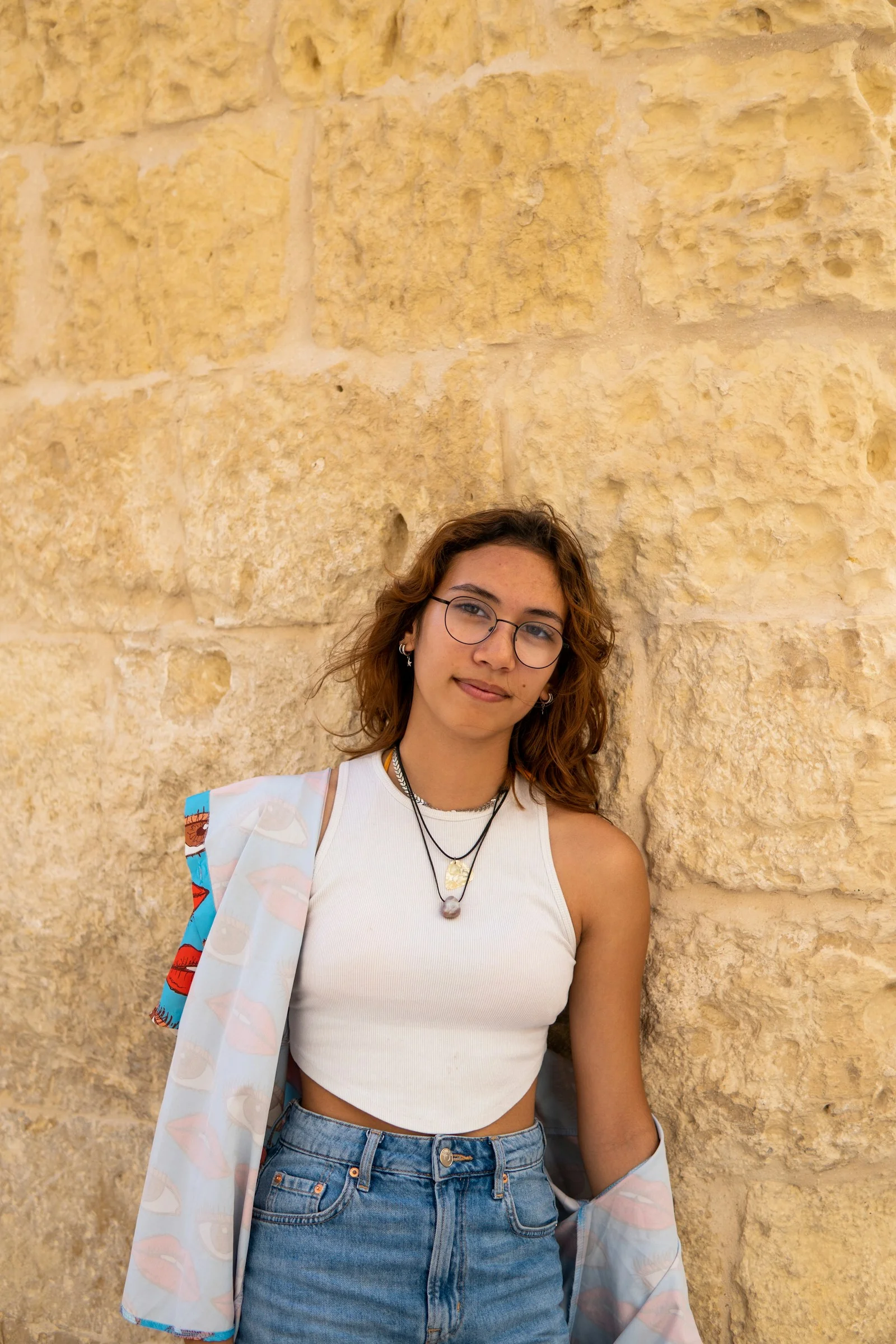 a woman wearing glasses leaning against a stone wall