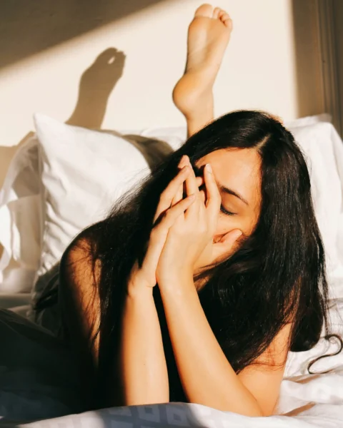 ベッドに横たわり顔に手を当てている女性