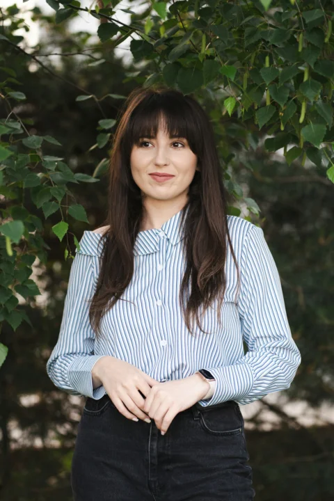 Woman smiles while posing near foliage