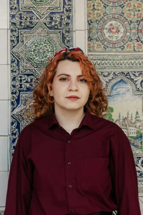 A woman with curly red hair and a patterned headband in a maroon shirt