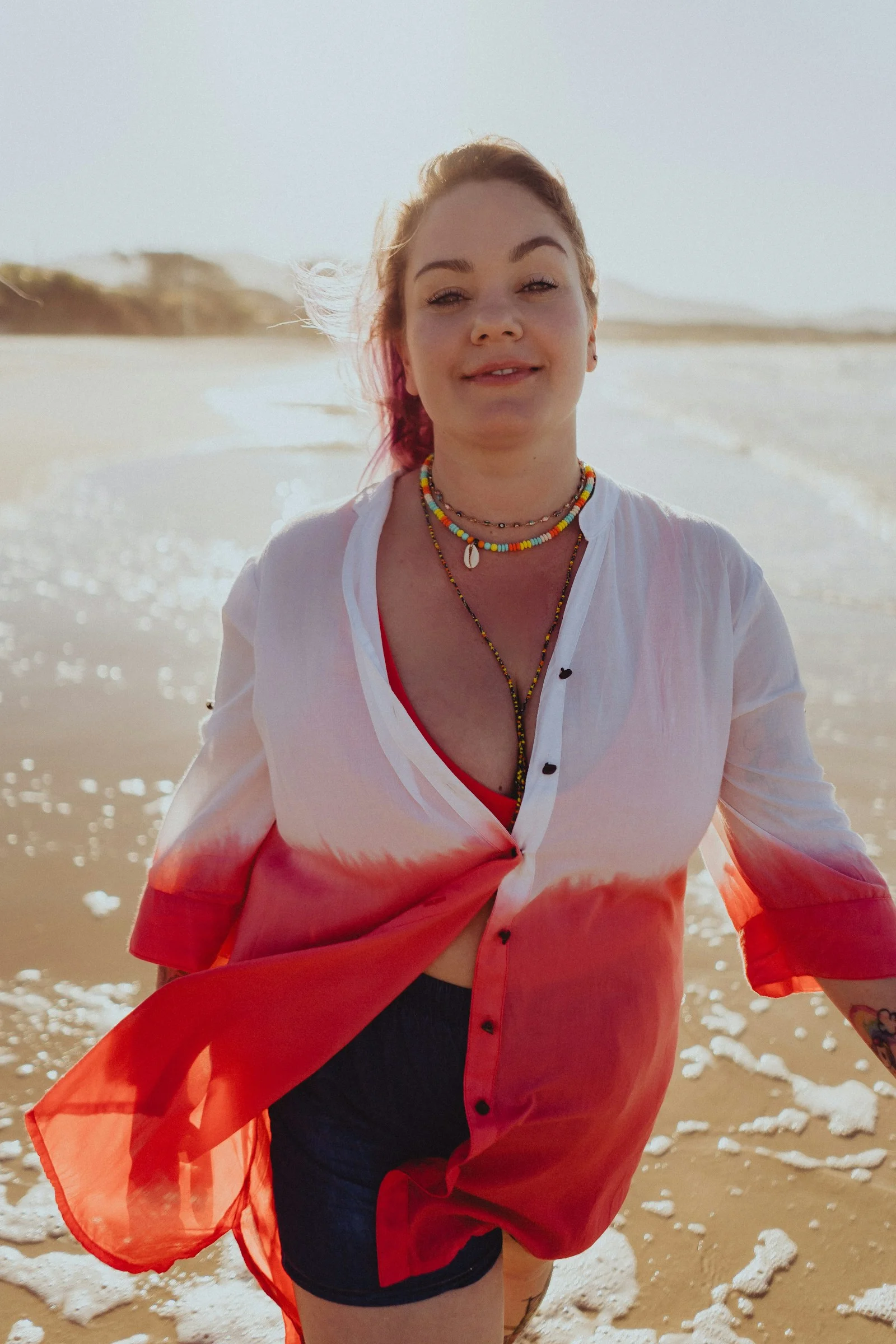 a woman standing on a beach with a red scarf around her neck