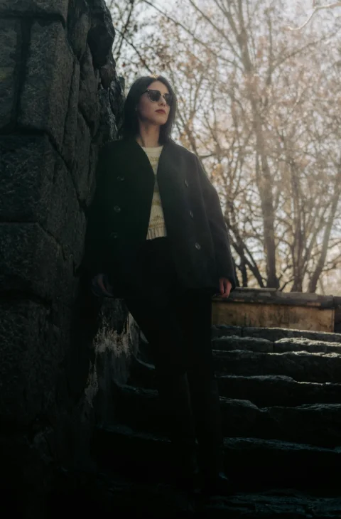A stylish woman poses next to a stone wall