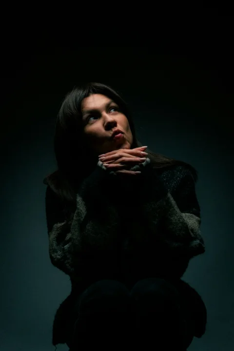 A woman sitting in the dark with her hands on her chest