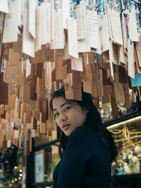 身穿深蓝色长袖上衣的女子站在悬挂的木牌下方